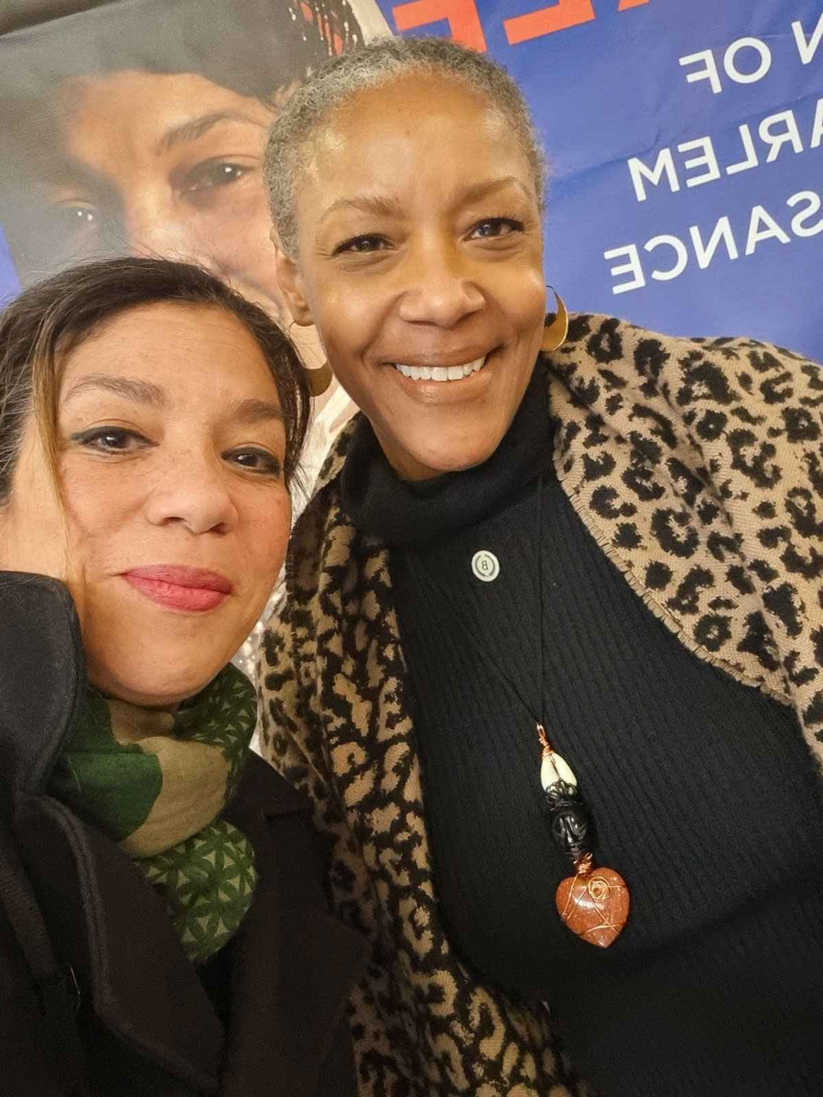 Two women smile in front of a poster